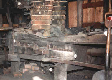 A wooden hearth with a cinder bed supports the fire.